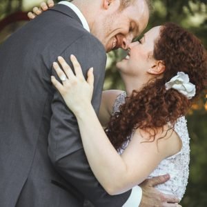 A couple, dressed in wedding attire, embrace and smile at each other.