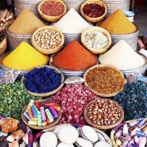 An assortment of spices and dried goods in baskets, including various powders, beans, and colorful items, are displayed at a market stall.