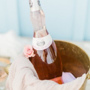 A bottle of pink wine sits in a brass bucket adorned with a pink rose and a white cloth.