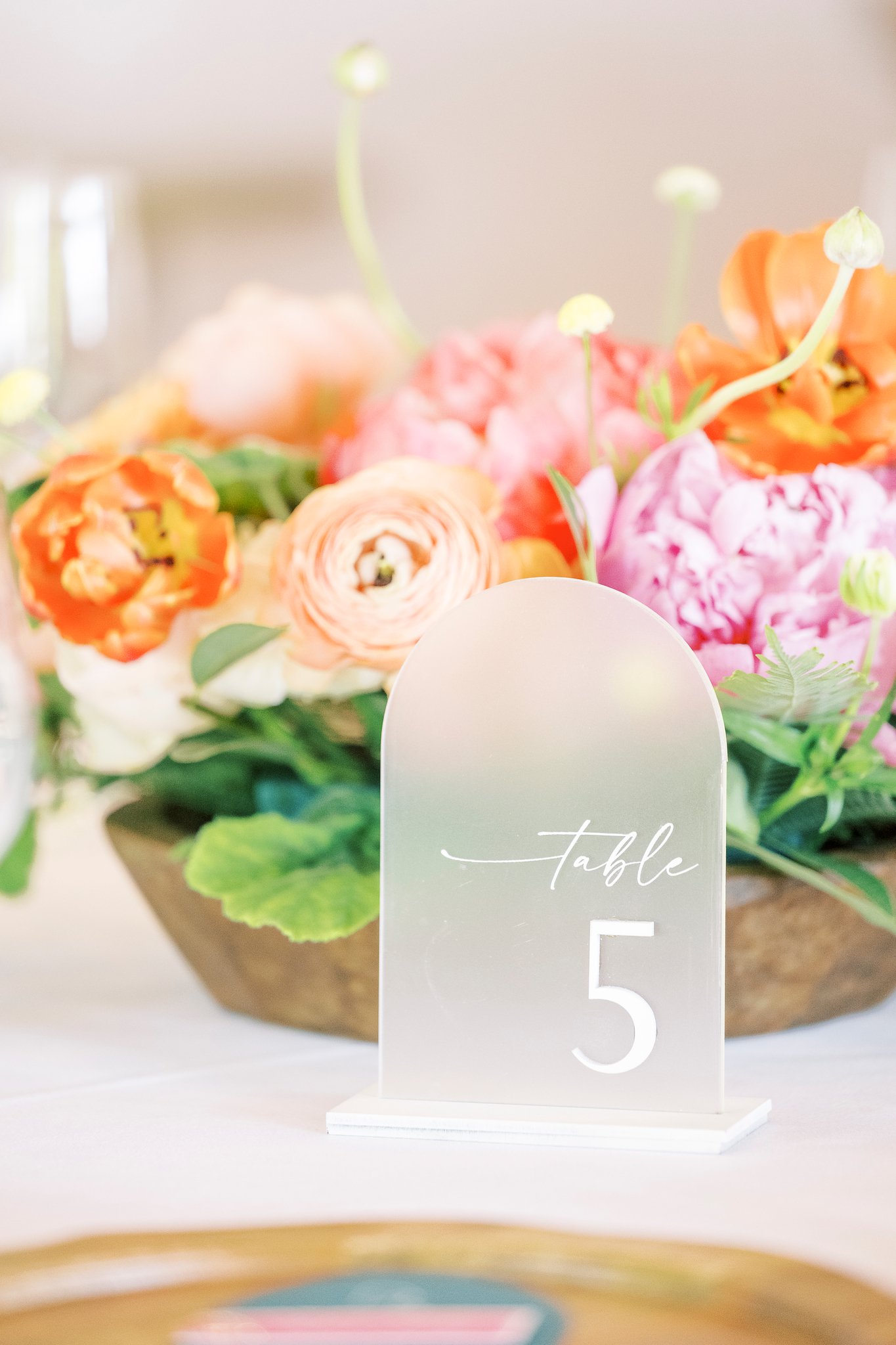 A table number sign labeled "Table 5" stands in front of a floral centerpiece with pink and orange flowers.