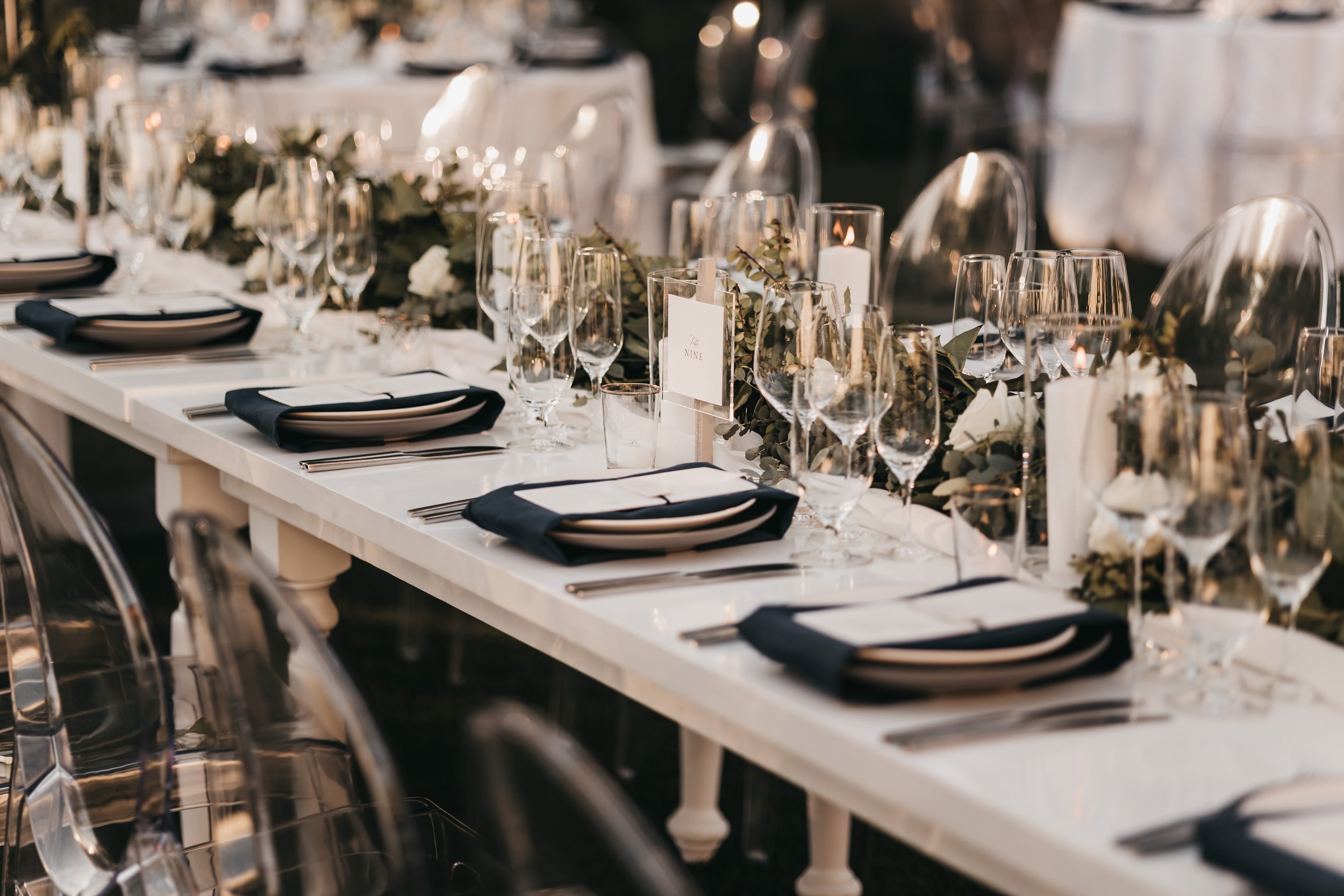 An elegantly set dining table with white plates, black napkins, various glasses, silverware, and floral centerpieces arranged for an event.