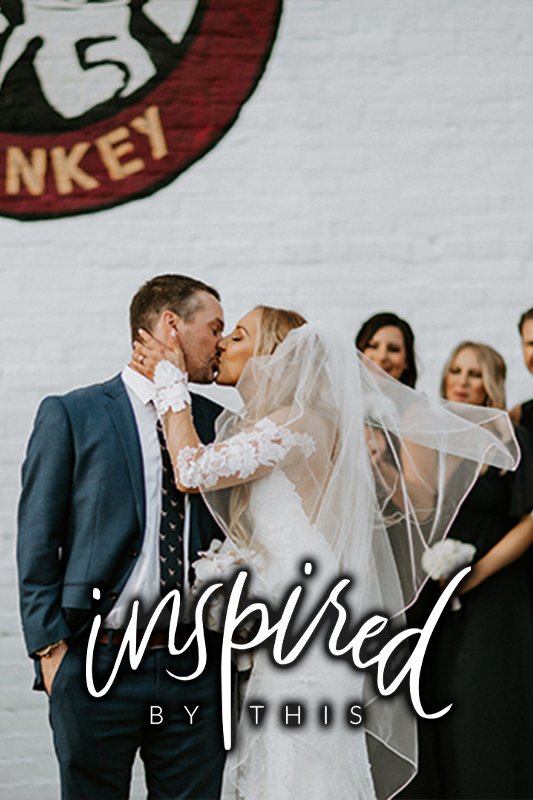 A bride and groom share a kiss in front of a group of people, with "Inspired by This" text overlaying the image.