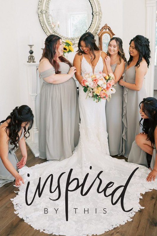 A bride in a white dress holds a bouquet while five bridesmaids in grey dresses gather around her, adjusting her gown's train in a well-lit room with a large mirror and decor. Text reads "Inspired by This.