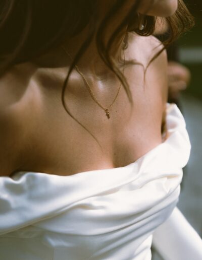 Close-up of a person wearing an off-shoulder white dress and a delicate gold necklace with a small cross pendant.