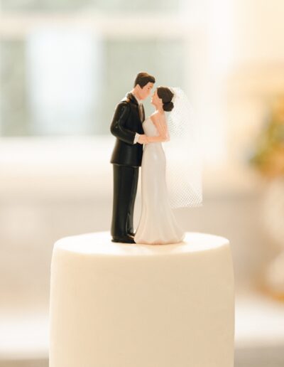 A wedding cake topper featuring a bride in a white dress with a veil and a groom in a black tuxedo standing close and holding each other.