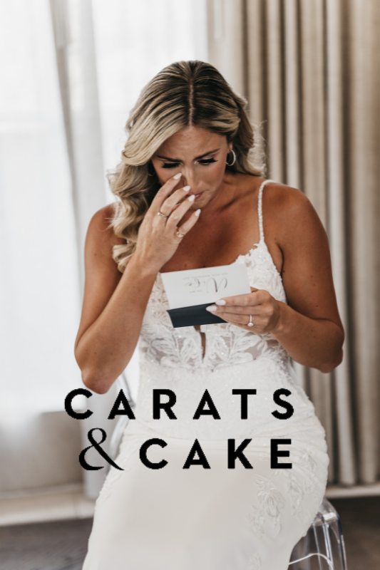 A bride in a white dress sits, reading a note and tearing up, next to the words "CARATS & CAKE.