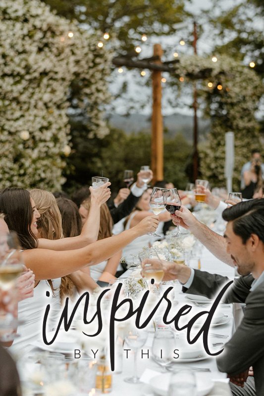 A group of people seated at a long table outdoors, raising their glasses in a toast. The scene is festive with string lights and greenery. The words "inspired by this" are overlaid on the image.