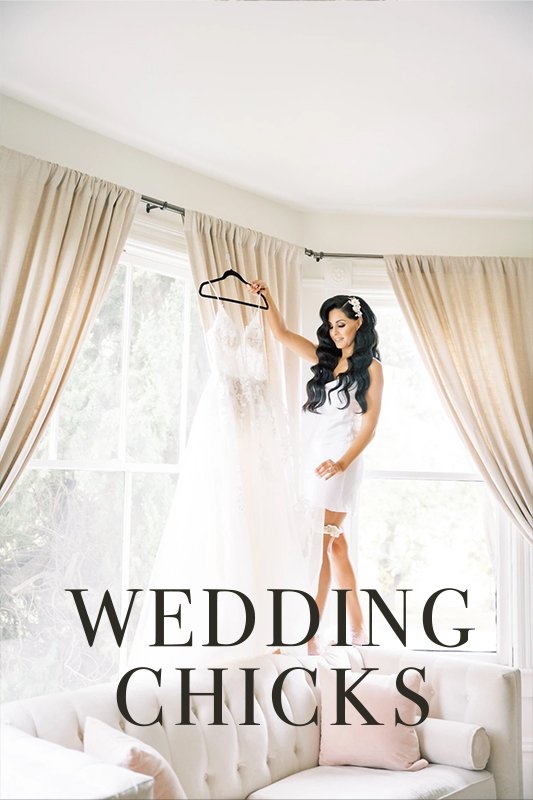 A woman wearing bridal attire stands on a sofa and reaches for a wedding dress hanging from a curtain rod. "WEDDING CHICKS" is written at the bottom of the image.