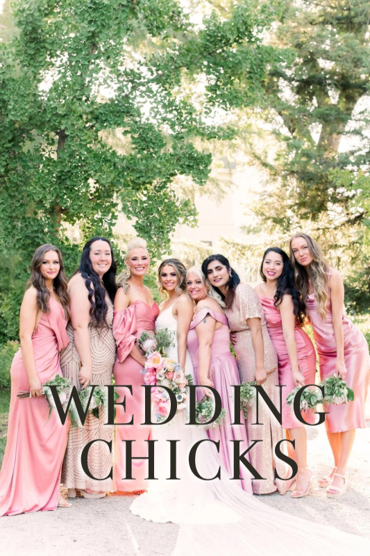 A bride in a white dress stands with seven bridesmaids in pink and peach dresses, posing outdoors in front of trees. Text overlay reads "WEDDING CHICKS.