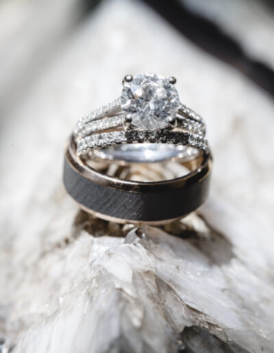 A diamond engagement ring and a wedding band are positioned on a textured surface.