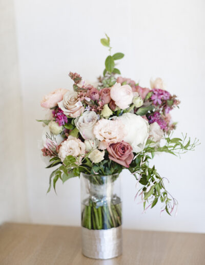 A bouquet of pink and white roses with green leaves in a clear vase on a wooden surface.