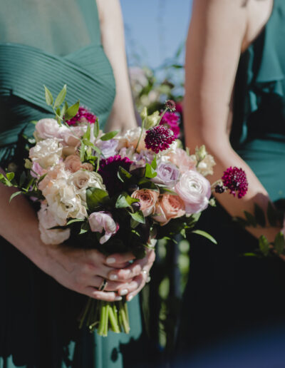 Three people wearing green dresses holding colorful bouquets with pink, white, and burgundy flowers.