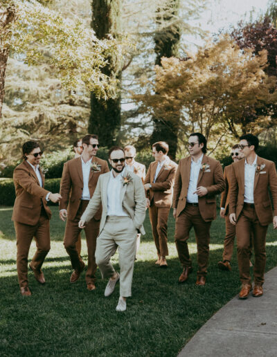 A group of men in suits, with one in a light suit, walk on grass surrounded by trees.