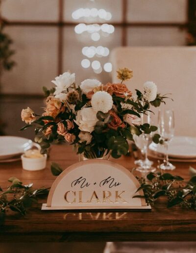 Elegant wedding table setting with a floral centerpiece, candles, plates, and a "Mr. & Mrs. Clark" sign.