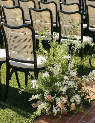 Rows of black chairs on a grass aisle with a floral arrangement of white and pink flowers at the front.