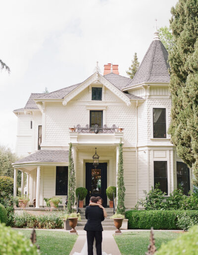 A couple embraces in front of the elegant, two-story Victorian-style house at Park Winters, surrounded by manicured gardens.