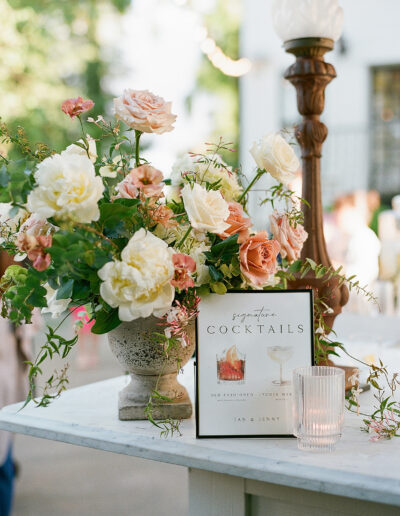 A delicate floral arrangement graces the table beside a cocktail menu, with a glass of water shimmering in the outdoor setting, capturing the enchanting essence of Park Winters weddings.