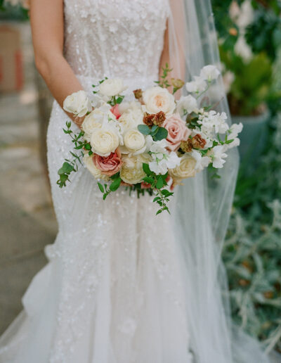 At Park Winters Weddings, a bride in a white lace dress gracefully holds a bouquet of white, pink, and peach flowers.