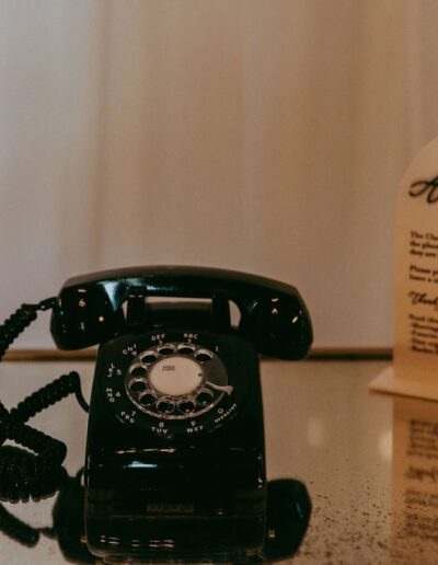 A black rotary phone on a glass surface next to a lit candle and a printed card with text.