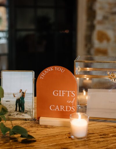 Table with a glass box for gifts and cards, a framed photo, a "Thank You" sign, flowers, and lit candles.