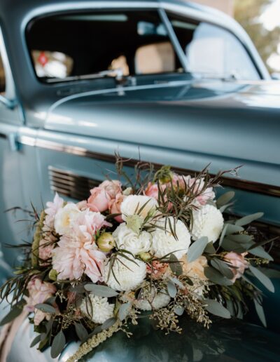 A vintage blue car with a bouquet of pink and white flowers on the hood.