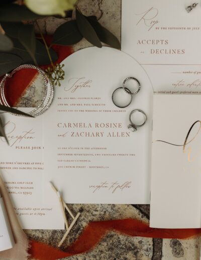 Wedding invitation set with RSVP card, two rings, and an envelope, displayed on a textured surface. Invitation for Carmela Rosine and Zachary Allen at Catalina Golf Club.