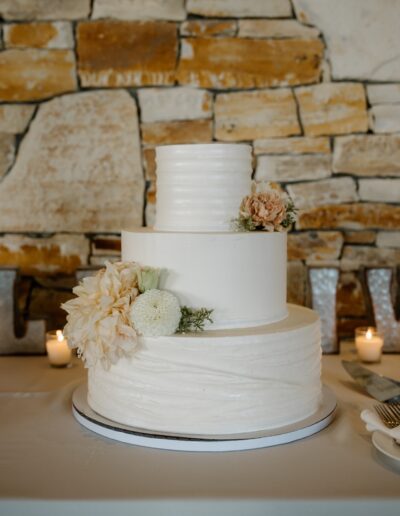 Three-tier white cake decorated with flowers, against a stone wall background.