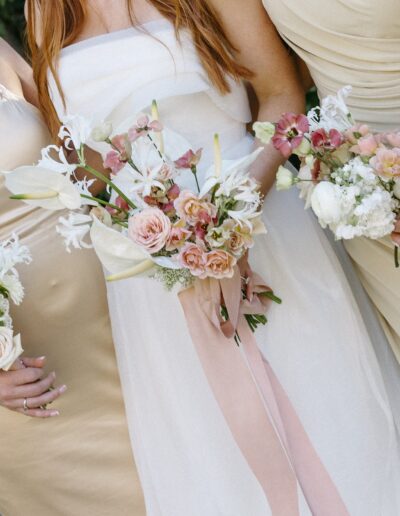 Three women in light-colored dresses hold bouquets of pastel flowers.