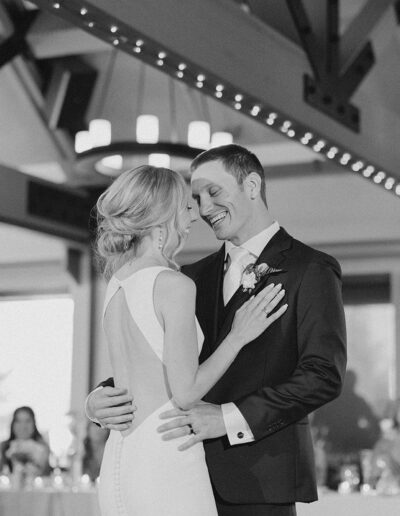 A couple in formal attire is dancing in a large hall with guests seated in the background.