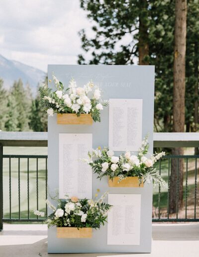 Wedding seating chart displayed outdoors with floral arrangements and a backdrop of trees and mountains.