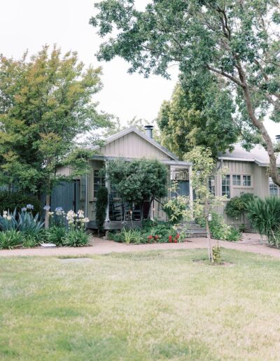 A quaint house with a front porch is surrounded by lush greenery and trees.