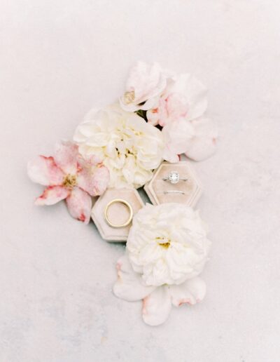 Rings in hexagonal boxes surrounded by white and pink flowers on a light background.