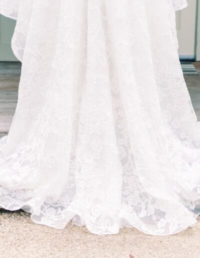 A white lace wedding dress train drapes over wooden steps, surrounded by small pink and white flowers.