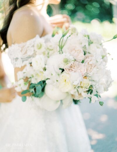 Bride in a white lace dress holding a bouquet of white and pale pink flowers.