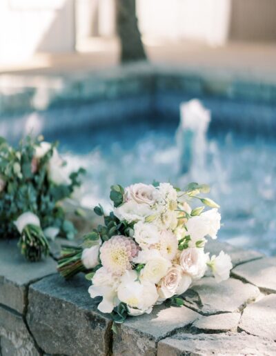 Bouquet of white and pale pink flowers resting on a stone ledge by a fountain.