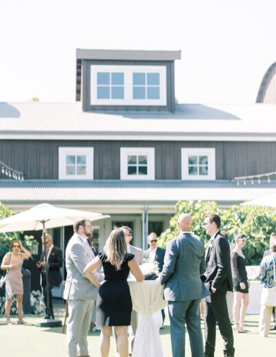 A group of people in formal attire stand and talk outside in front of a large building with multiple windows.