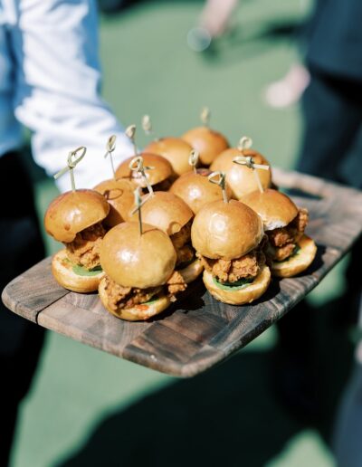 A tray of mini chicken sandwiches with toothpicks is being served outdoors.