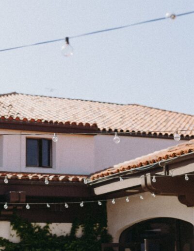 A courtyard with string lights hanging above, surrounded by buildings with terracotta roofs and white walls under a clear blue sky.