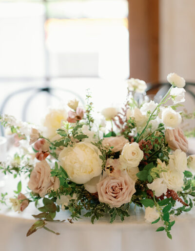 A floral centerpiece with white, cream, and pale pink flowers graces a round table at Park Winters Weddings, surrounded by empty wine glasses and small clear containers.