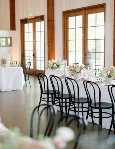 An elegant indoor Park Winters Weddings reception features round tables adorned with white linens, floral centerpieces, and black chairs. French doors and wooden beams enhance the rustic charm, creating a magical atmosphere.