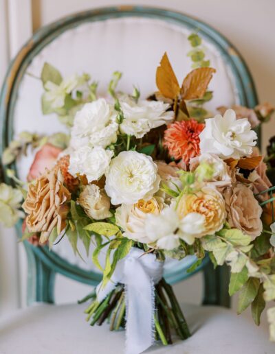 A bouquet of assorted flowers, including white and peach roses, sits on a teal chair with a white cushion.