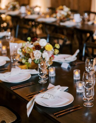 Elegant dinner table with white plates, folded napkins, wine glasses, candles, and a floral centerpiece.