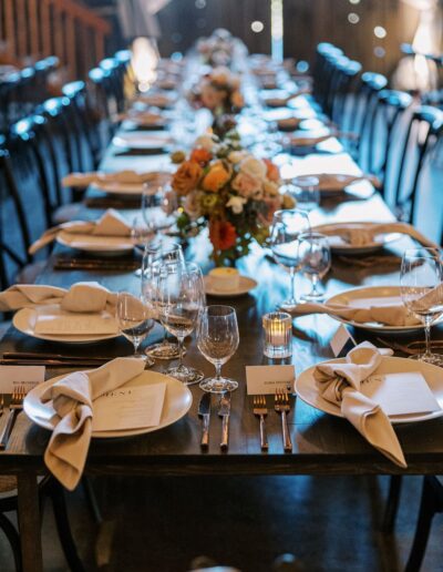 A long dining table set with plates, glasses, cutlery, and folded napkins. Floral centerpieces line the middle of the table.