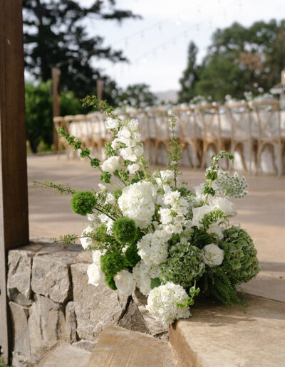 Bouquet of white and green flowers arranged on stone steps, with a blurred outdoor dining area in the background.