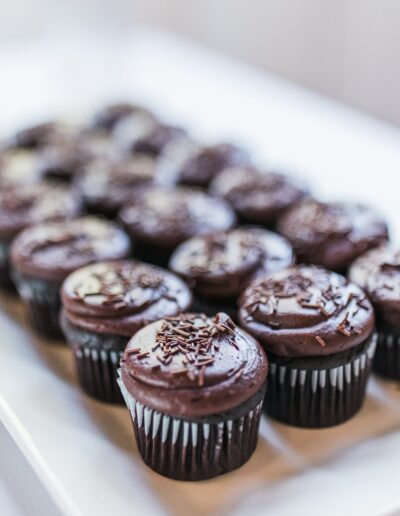 A tray of chocolate cupcakes with sprinkles arranged neatly on a white surface.