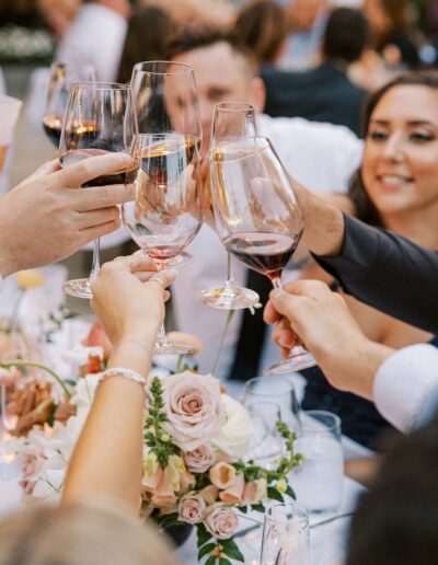 People clinking wine glasses at a table adorned with flowers and candles during a celebration.