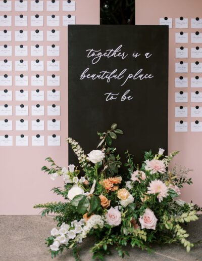 A black sign reads "together is a beautiful place to be," surrounded by pink card displays and floral arrangements.