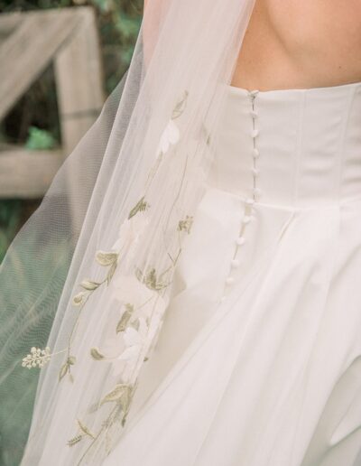 Close-up of a white wedding dress with floral embroidery on the veil and a row of buttons down the back.