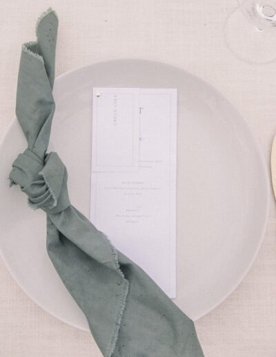 A white plate with a tied green napkin and a menu card. A fork and knife are placed on either side.