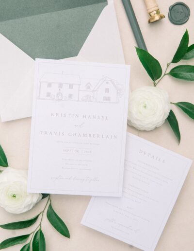 Wedding invitation with elegant typography and minimalistic house illustration, accompanied by greenery, white flowers, and an envelope.